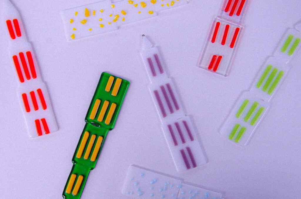 Op een witte tafel liggen enkele glazen domtorentjes (van de Domtoren in Utrecht). In verschillende designs als Groen, Gele spikkels, transparant met oranje, wit, rood en paars.