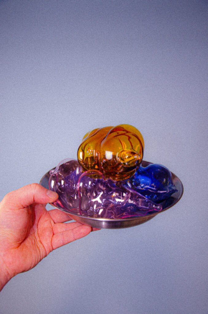 Hand houd aluminium bord vast met mondgeblazen borosilicaat glas in de kleuren amber, roze en blauw.