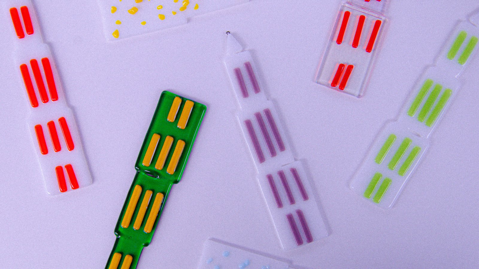 Op een witte tafel liggen enkele glazen domtorentjes (van de Domtoren in Utrecht). In verschillende designs als Groen, Gele spikkels, transparant met oranje, wit, rood en paars.
