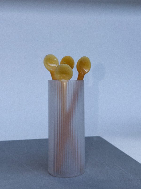Lang mat glas met enkele gele honing lepels er in.
